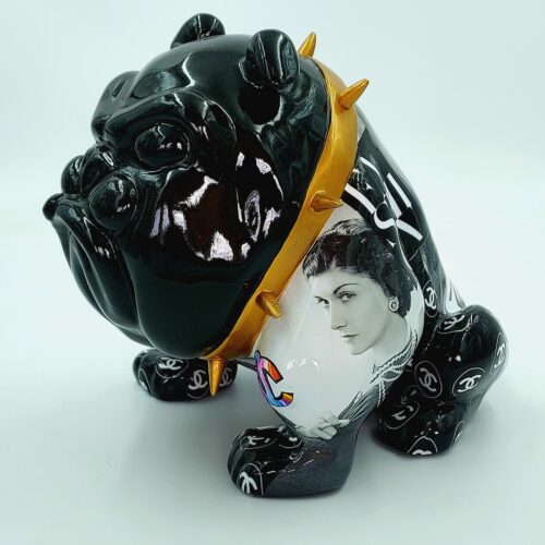 A black bulldog figurine with a gold spiked collar, featuring various designer logos and a monochrome portrait of a woman on its side.