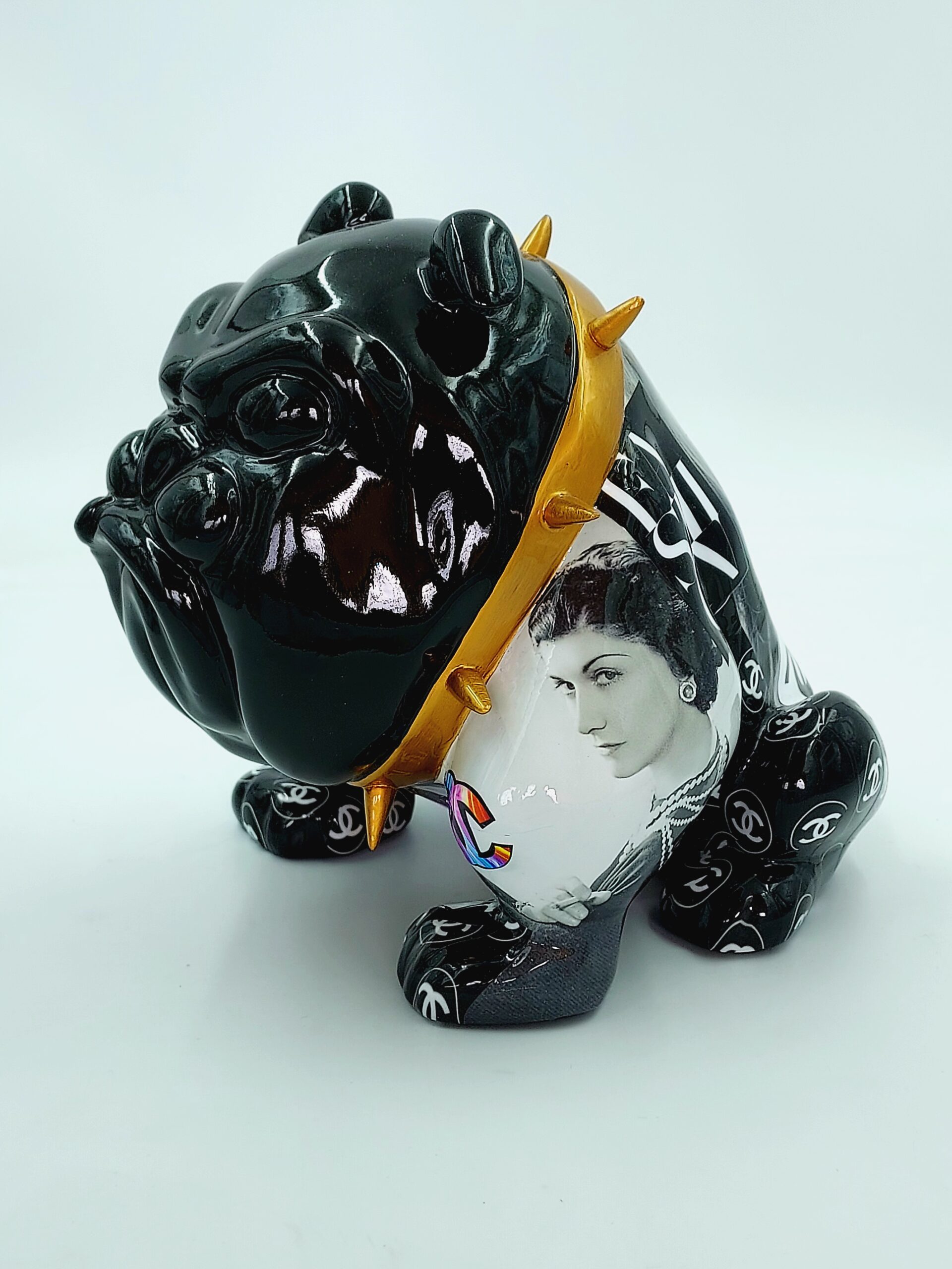 Bulldog Avella 55cm dog - Coco 1 A black bulldog figurine with a gold spiked collar, featuring various designer logos and a monochrome portrait of a woman on its side.