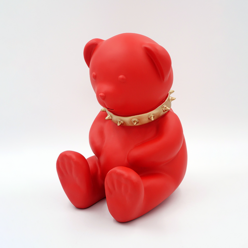 A red bear sculpture wearing a gold spiked collar, sitting against a white background.