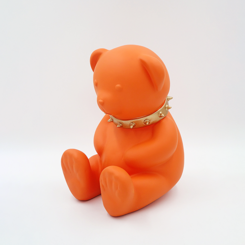 Orange teddy bear figurine wearing a spiked gold collar.