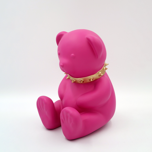 Pink teddy bear statue wearing a gold spiked collar.
