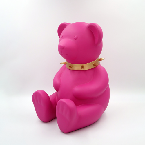 Pink teddy bear figurine wearing a gold spiked collar, sitting upright against a white background.
