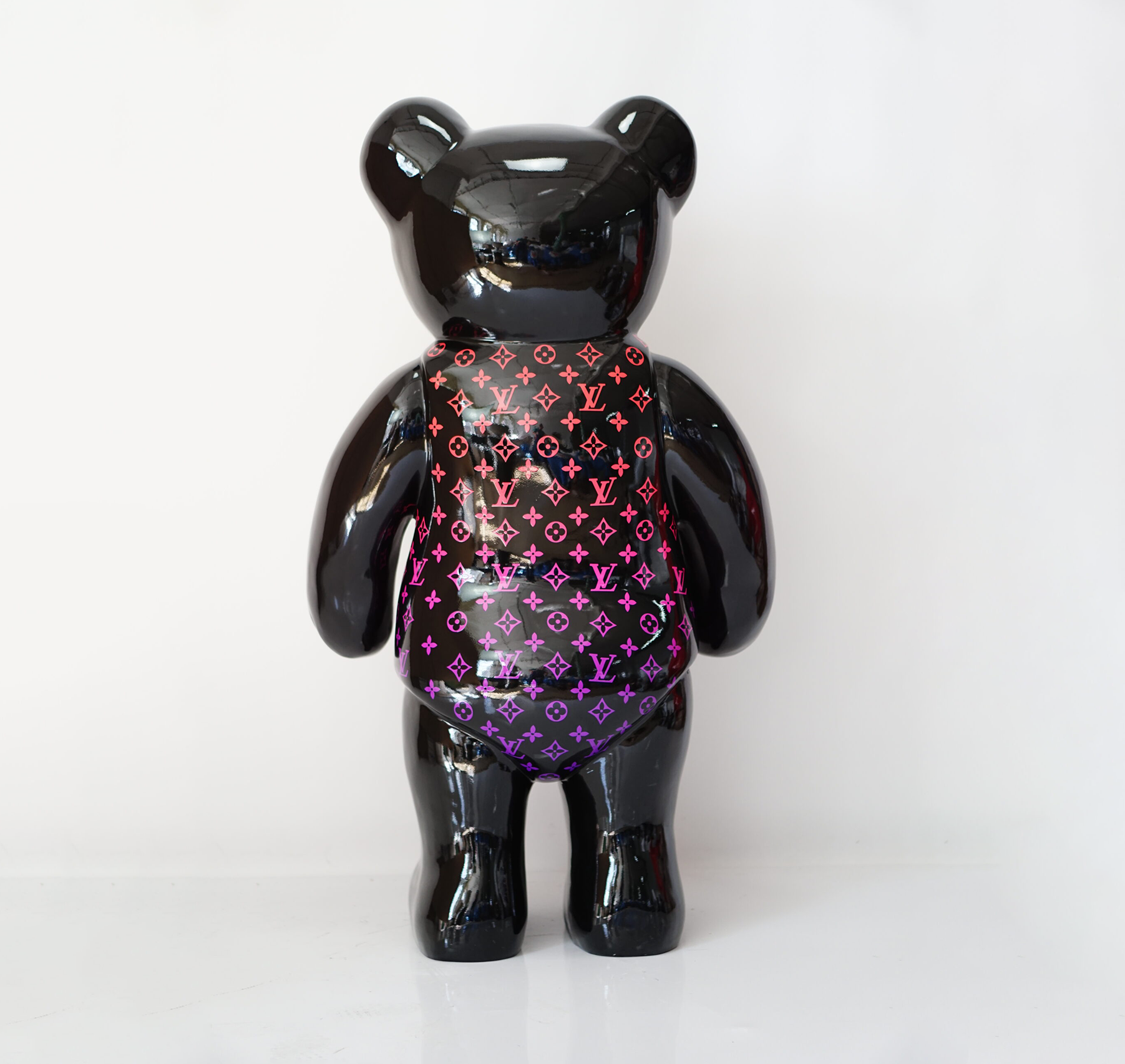 Standing teddy bear monogram - pink gradient 2 Black bear-shaped figurine with a gradient Louis Vuitton pattern on its back.
