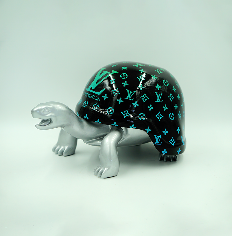 Turtle in Helmet with Monogram - Green Gradient 1 Silver turtle figurine with a black shell featuring turquoise Louis Vuitton logos.