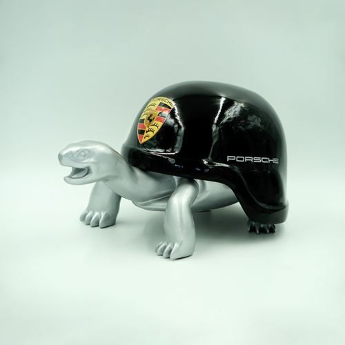 A turtle figurine with a shiny black shell featuring the Porsche logo and the word 