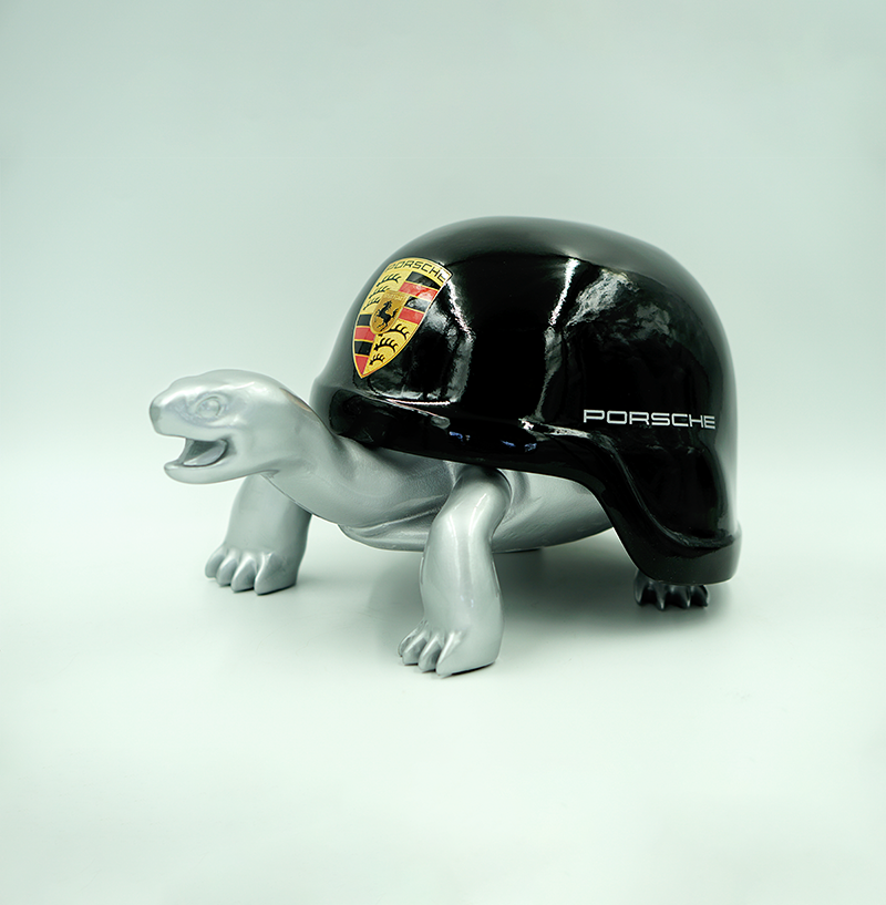 Turtle in a Helmet - Porsche 1 A turtle figurine with a shiny black shell featuring the Porsche logo and the word