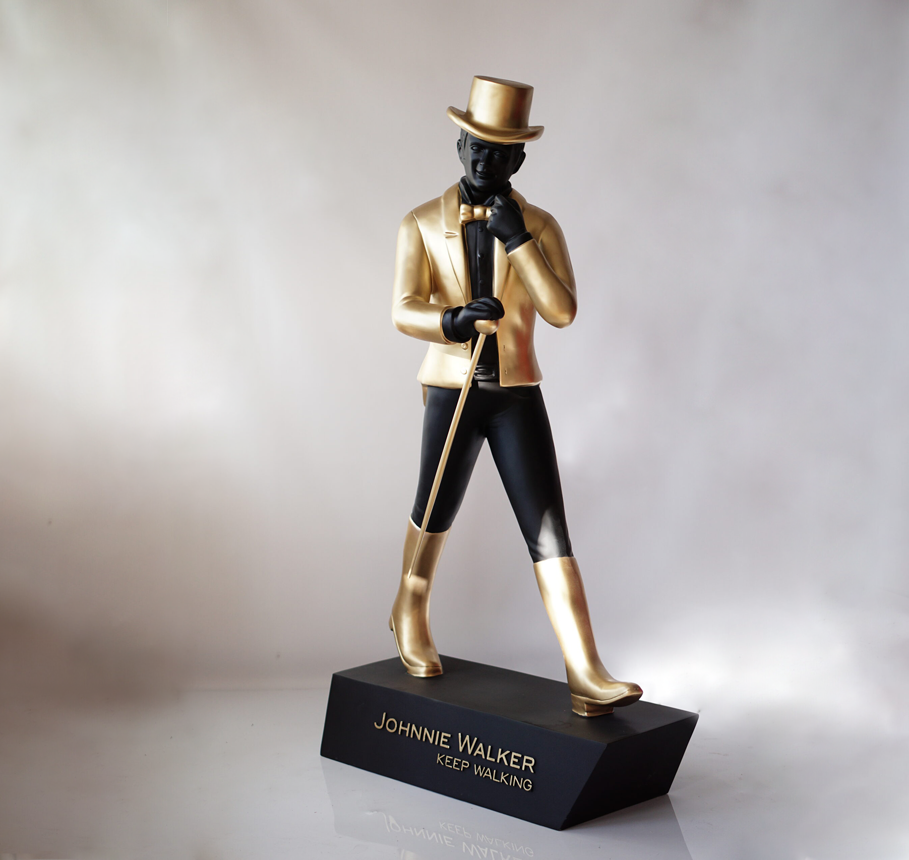 Johnnie Walker - keep walking 1 Statue of a man in black and gold clothing, holding a walking cane, standing on a black base with the inscription