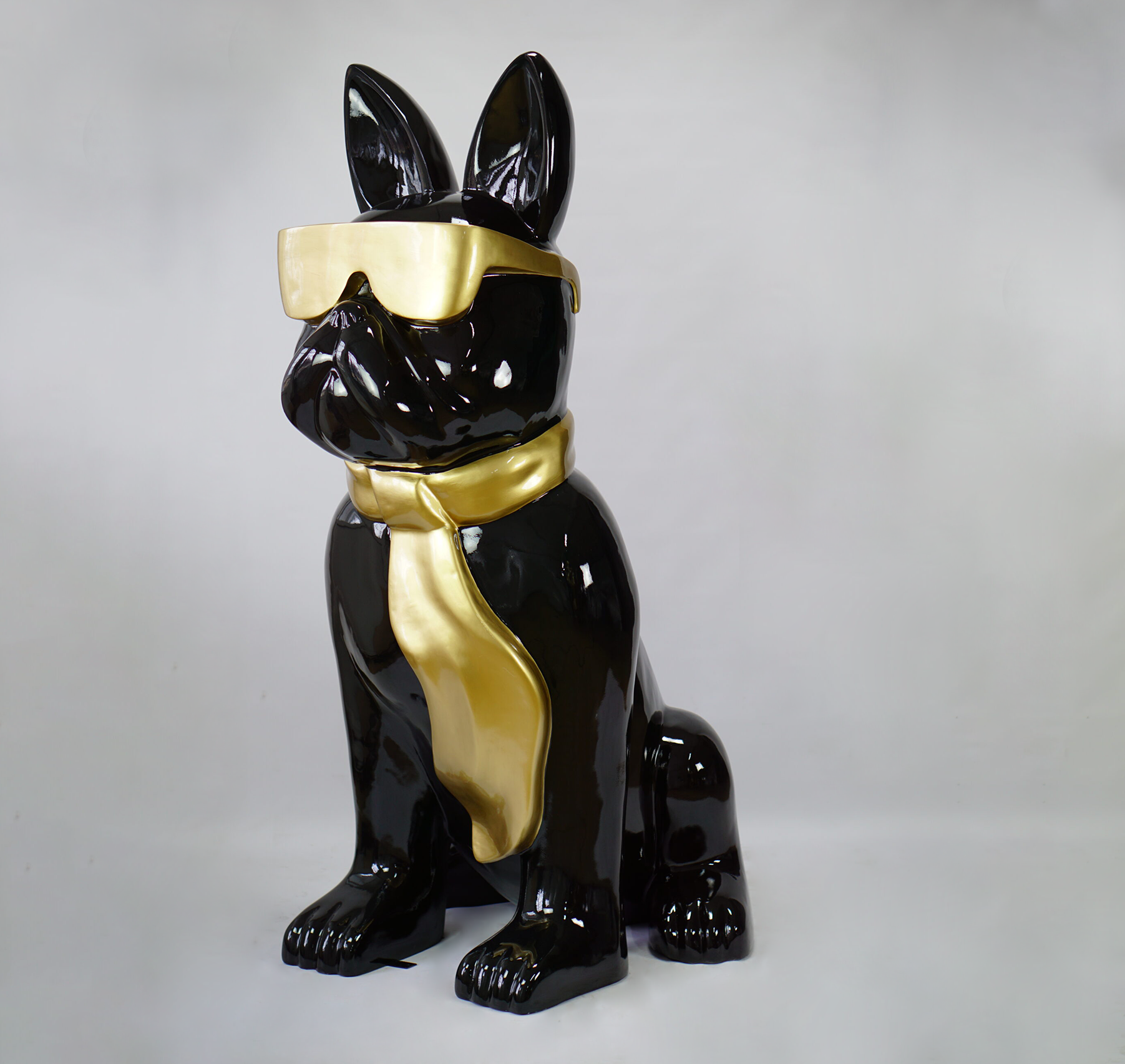 Large bulldog figure with tie and glasses - black gold 1 A glossy, black ceramic sculpture of a dog wearing gold sunglasses and a gold tie is set against a plain white background.