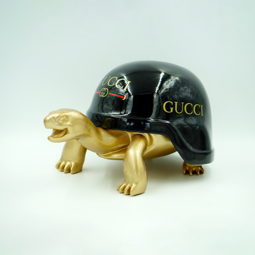 Golden turtle figurine with a black shell featuring the Gucci logo.