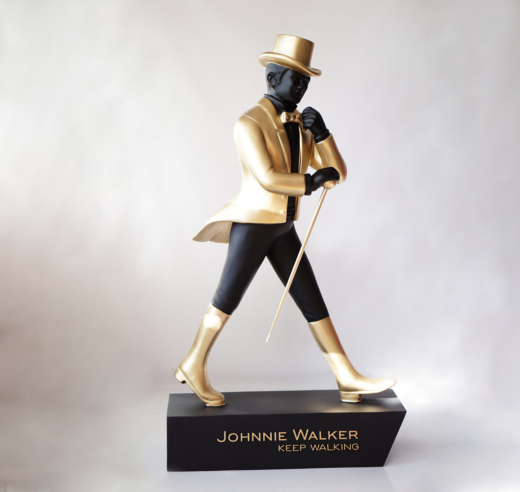 Johnnie Walker - keep walking 2 A statue of a man wearing a top hat, bowtie, and suit, walking with a cane. The statue is standing on a black base with the text