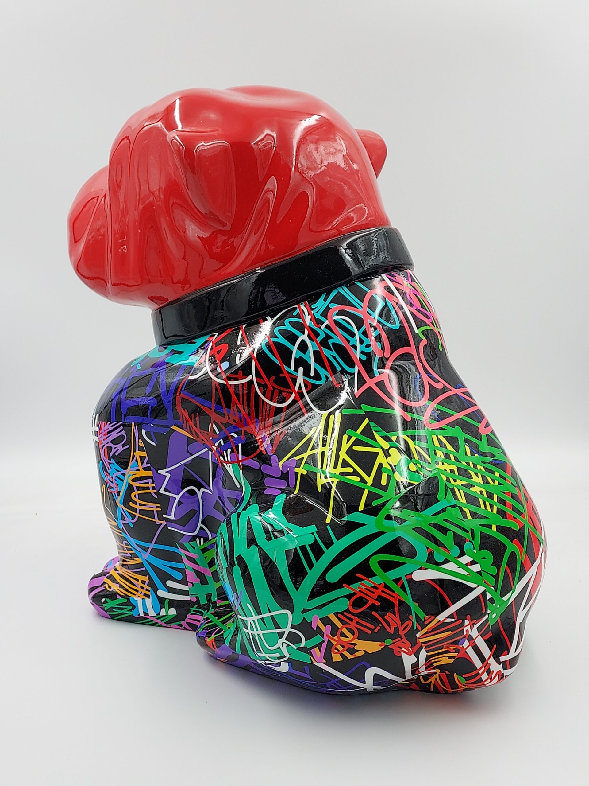 Bulldog Angelo 60cm dog - spray 3 A sculpture of a sitting dog with a red head and a black body covered in colorful graffiti-style writing and designs.