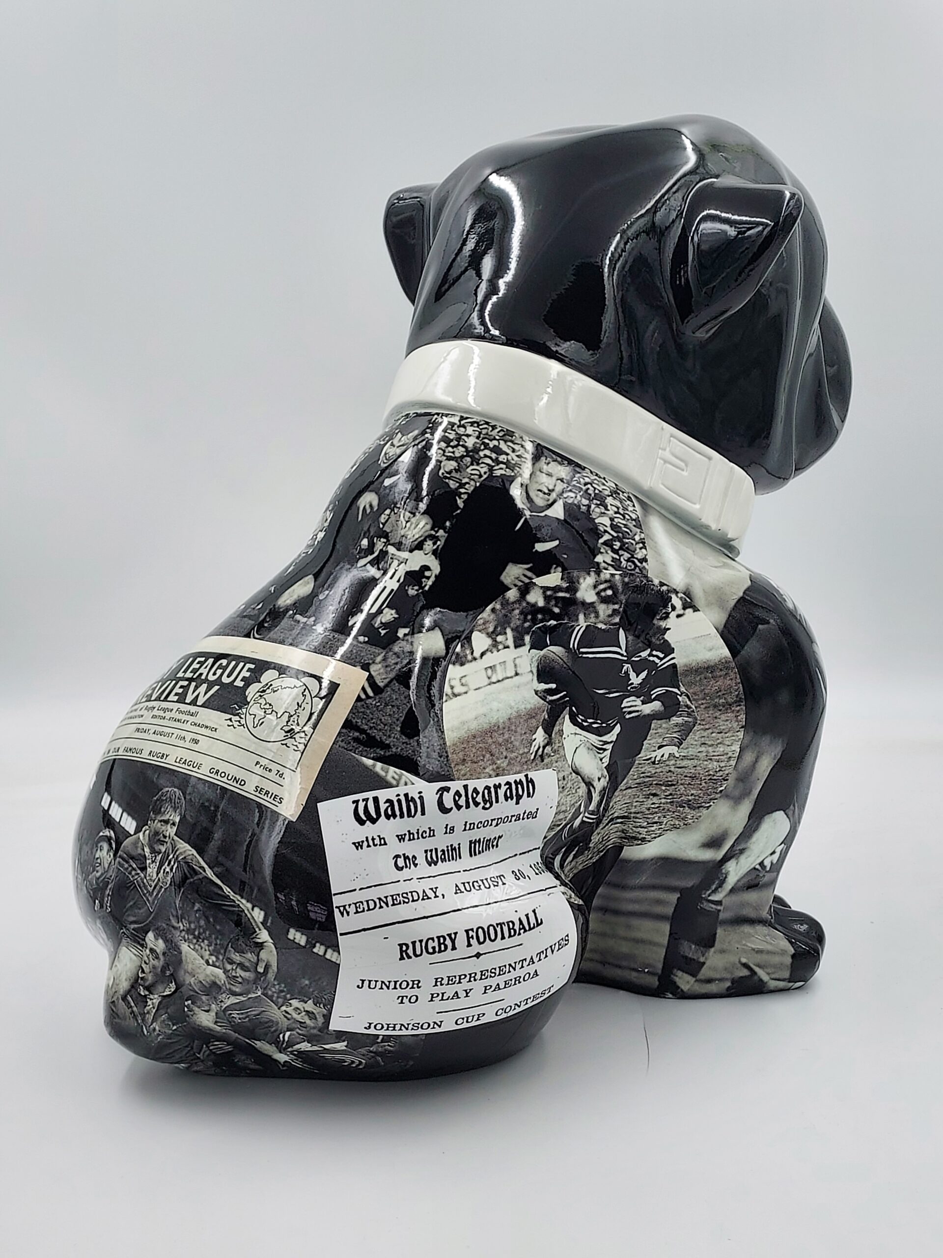Bulldog Angelo 60cm dog - rugby 3 Black ceramic bulldog figurine with vintage rugby-themed newspaper clippings and black-and-white images of players.