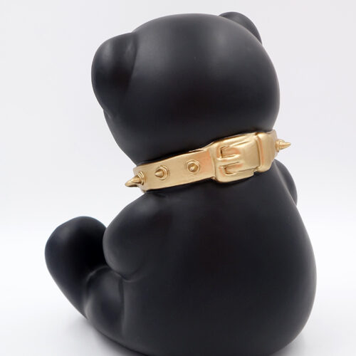 Black bear figurine wearing a gold spiked collar, facing away.