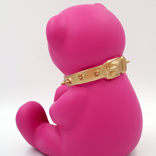Bright pink teddy bear figurine sitting, wearing a golden spiked collar.