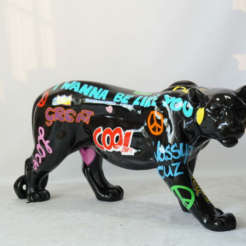 A black panther sculpture with colorful graffiti-style messages and symbols, including phrases like 