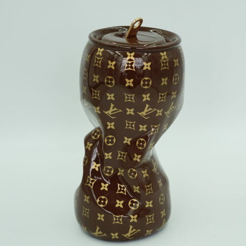 A distorted brown and gold ceramic jar with a Louis Vuitton monogram pattern and a lid with a small loop handle.