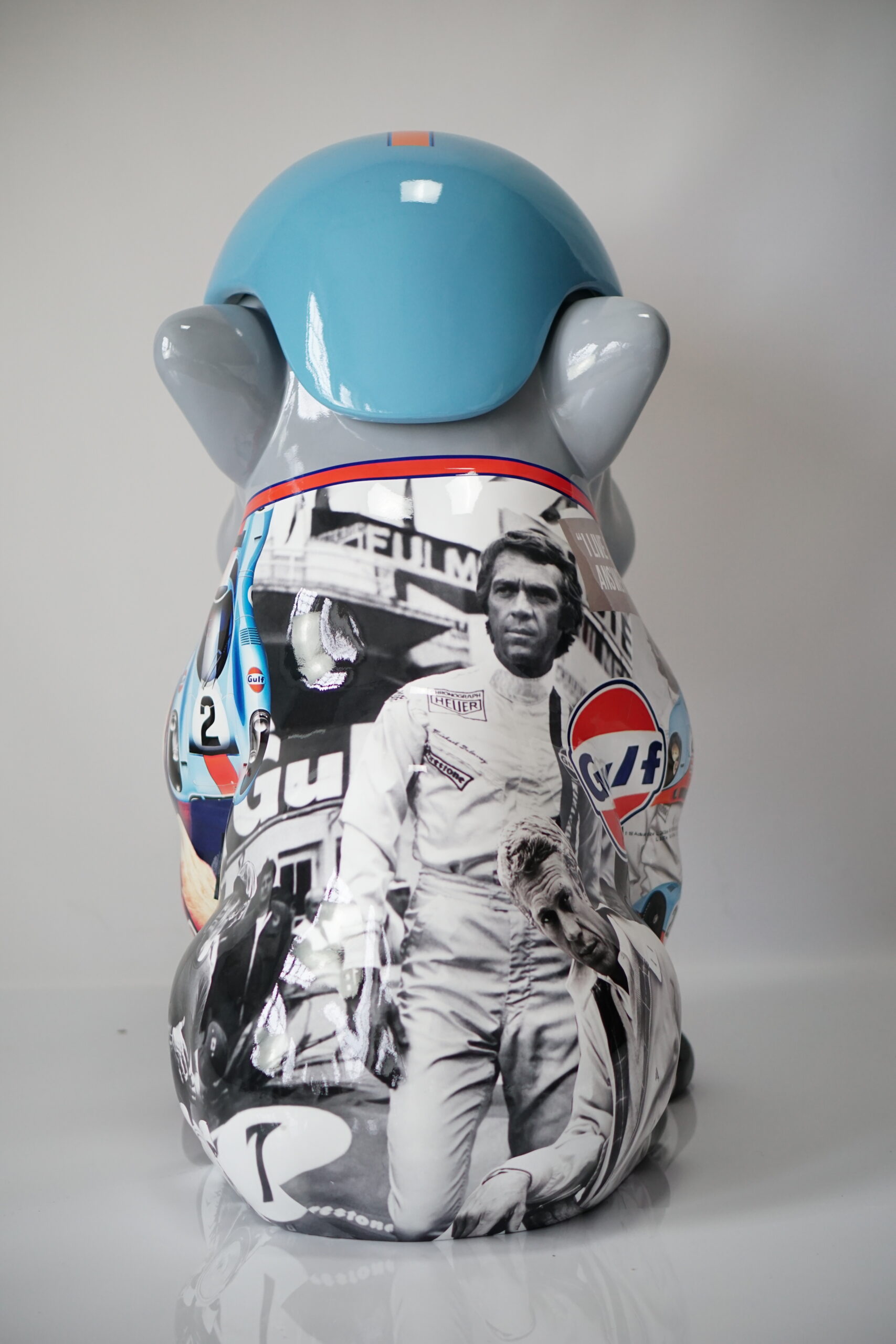 Bulldog dog with hat - McQueen 3 Sculpture of an animal painted with racing imagery and a blue helmet, featuring black and white pictures of drivers and Gulf branding.
