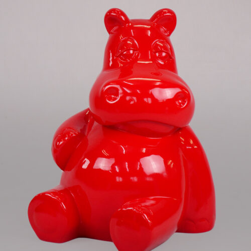 Glossy red hippopotamus-shaped sculpture sitting on a gray surface.