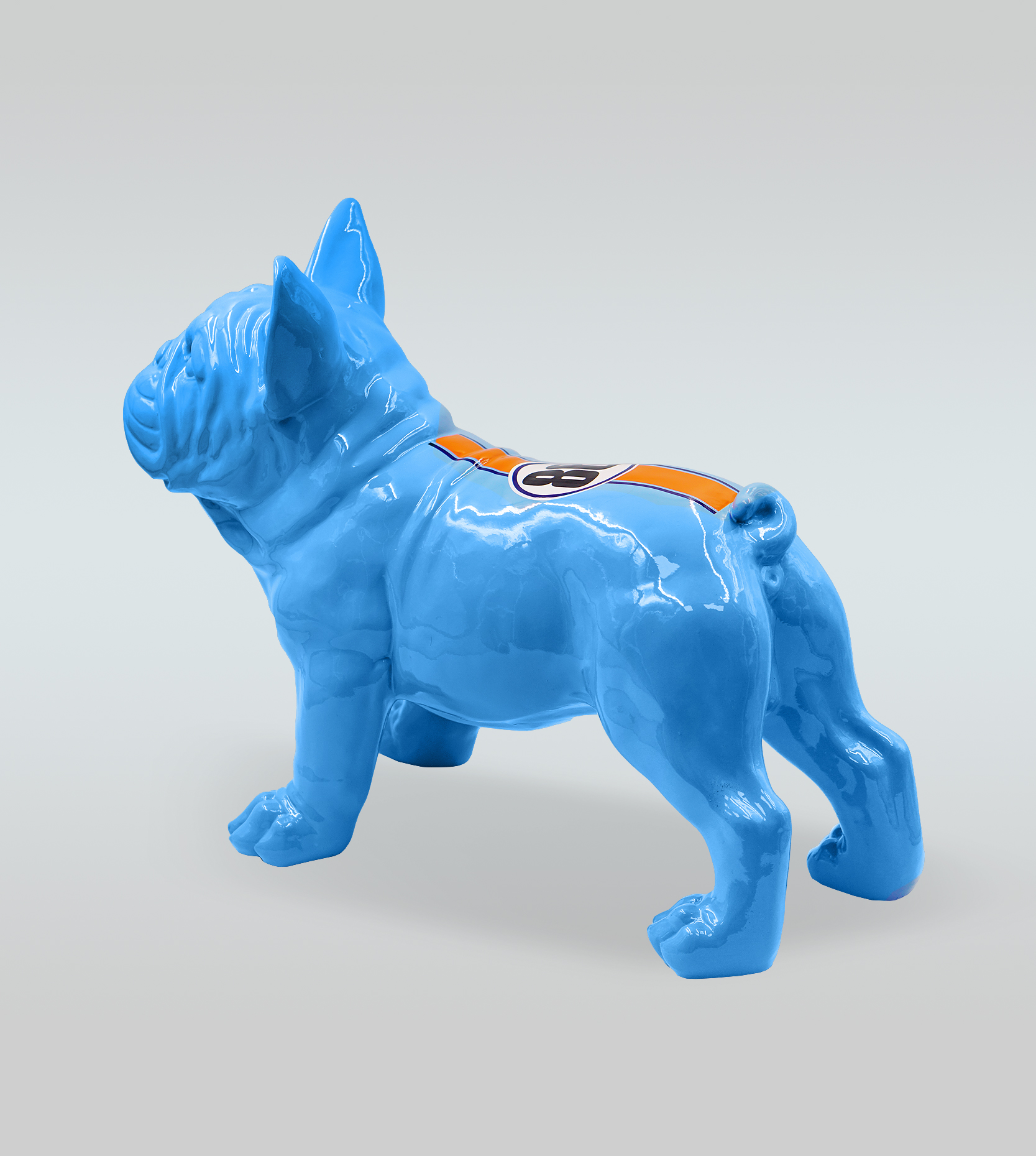 Bulldog Juki M Dog - Standing One Color + Sticker 2 Blue ceramic bulldog figure with an orange stripe and circular logo on its back.