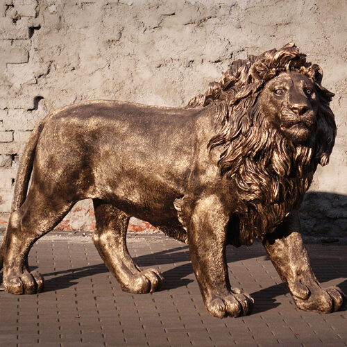 Bronze lion statue in front of a textured brick wall background.