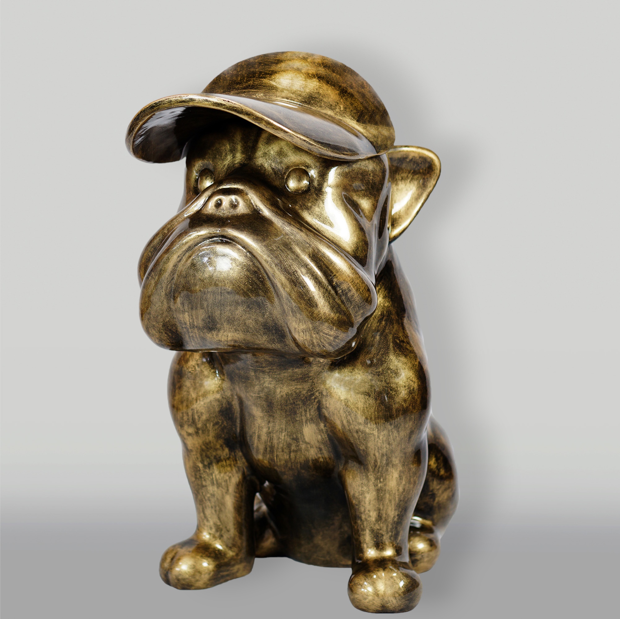 Dog Bulldog with Cap - Golden Patina 1 Bronze-colored sculpture of a sitting bulldog wearing a cap.