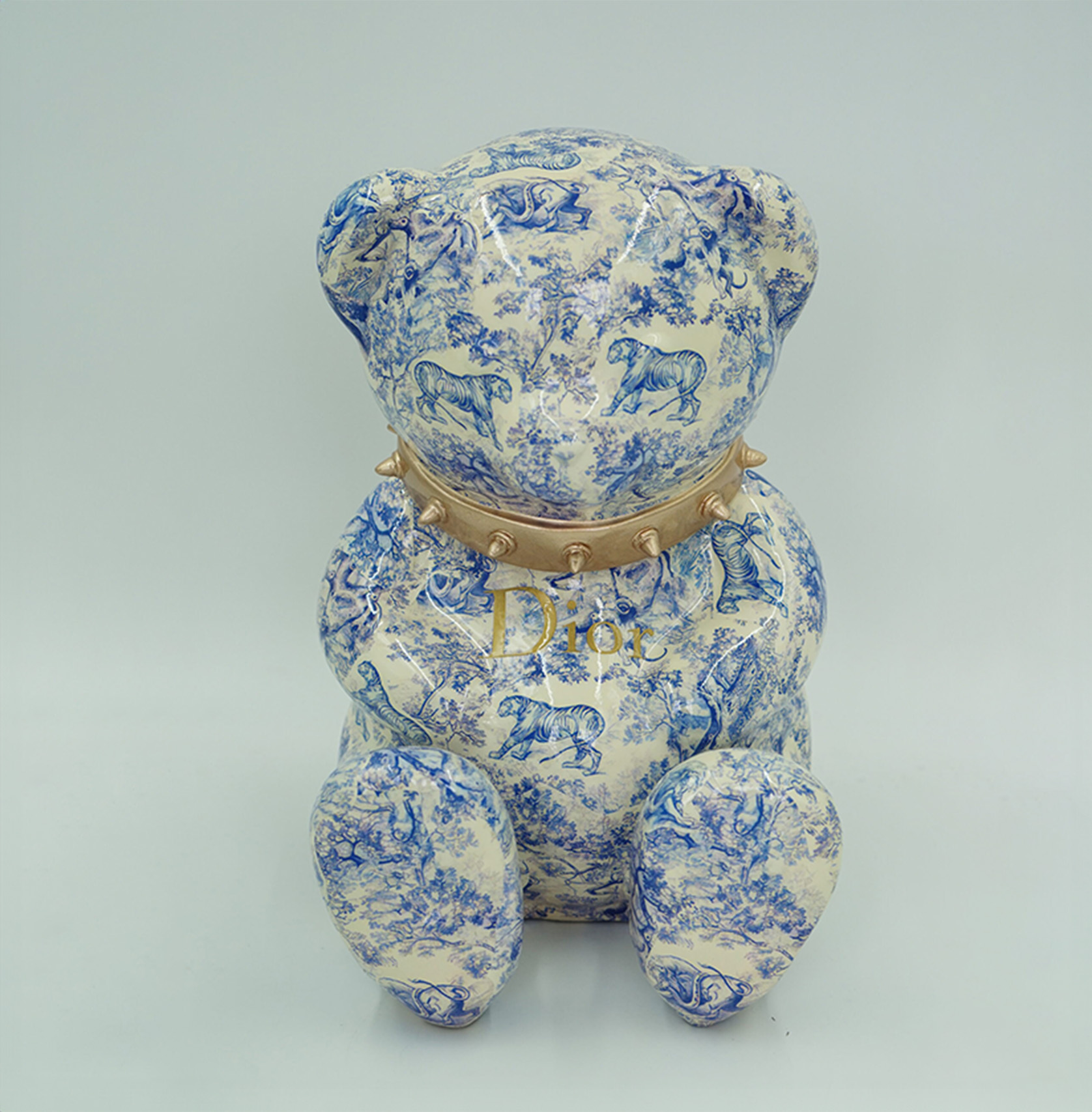 Bear D H-31cm 1 A ceramic bear figurine with a blue and white pattern featuring animals and nature scenes. The bear wears a gold collar with spikes, and the word