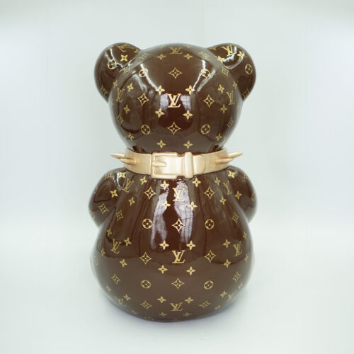 A brown figurine of a bear with a glossy finish, adorned with a gold Louis Vuitton monogram pattern, and wearing a gold spiked collar.