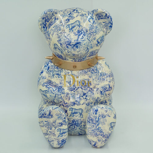 A ceramic bear statue with blue animal and foliage patterns, wearing a leather collar with gold-colored spikes and the word