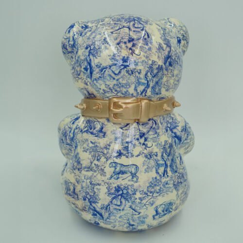 There are no Polish words written on the object in the image. It depicts a bear figure with intricate blue illustrations of animals and scenes, wearing a gold studded collar.