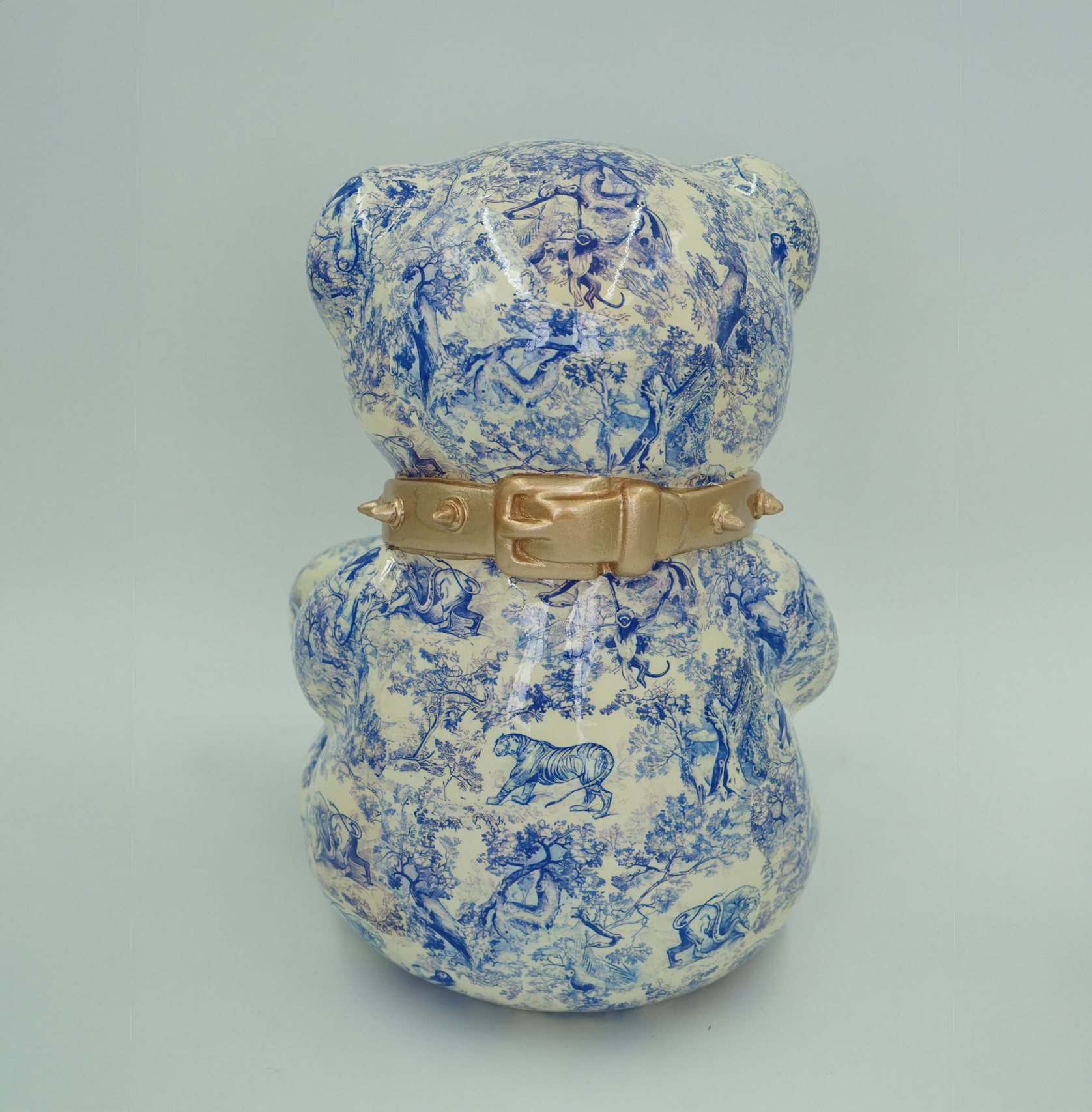 Bear D H-31cm 2 I don't recognize any text in Polish in the provided image. The image shows the back of a ceramic bear figurine with a blue pastoral print pattern and a gold-colored collar.
