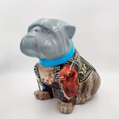A painted sculpture of a seated bulldog with a glossy grey head, a blue collar, and a body featuring collage-style artwork with various printed images and text.