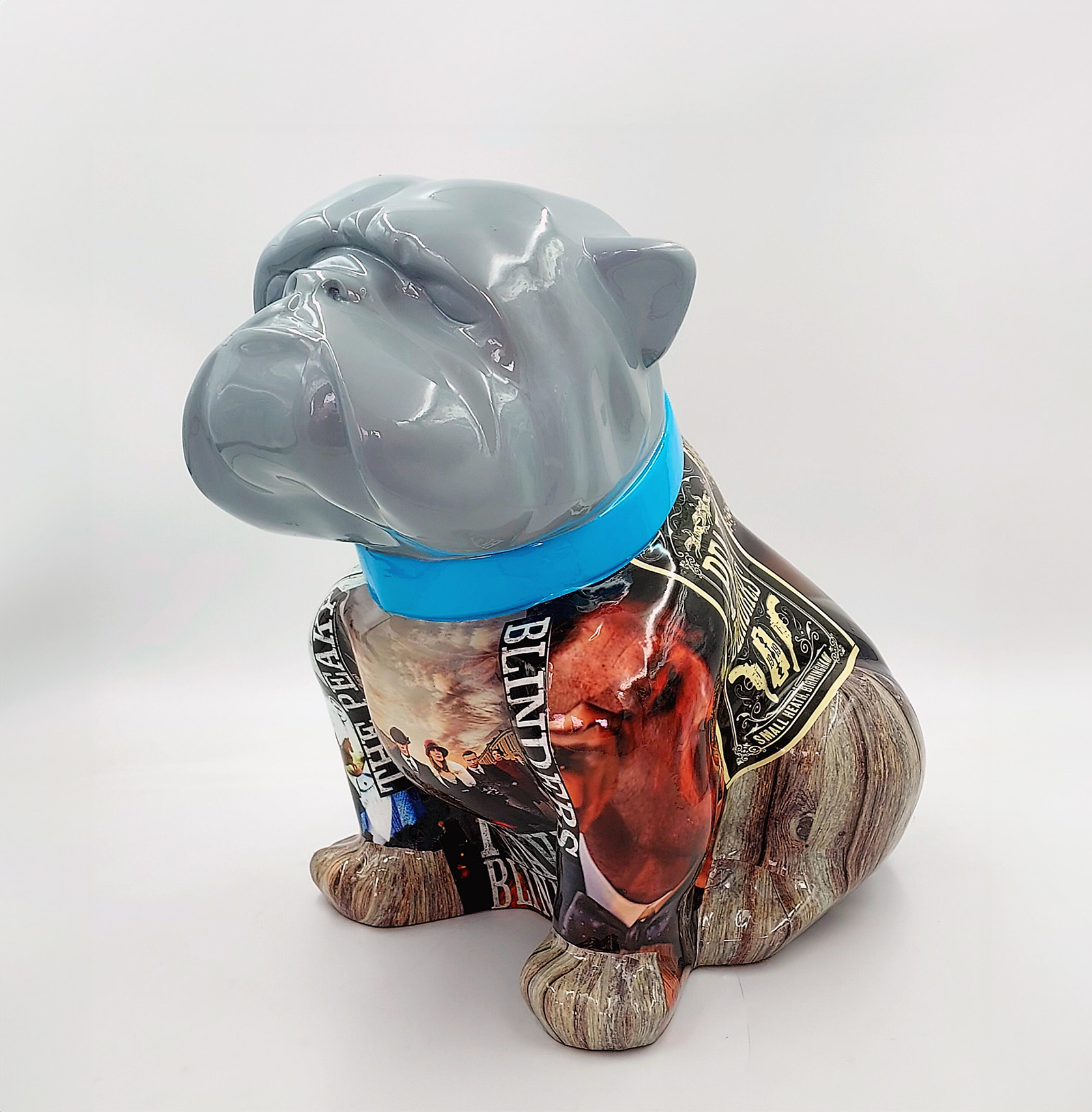 Bulldog Angelo 40cm dog - Peaky Blinders 1 A painted sculpture of a seated bulldog with a glossy grey head, a blue collar, and a body featuring collage-style artwork with various printed images and text.