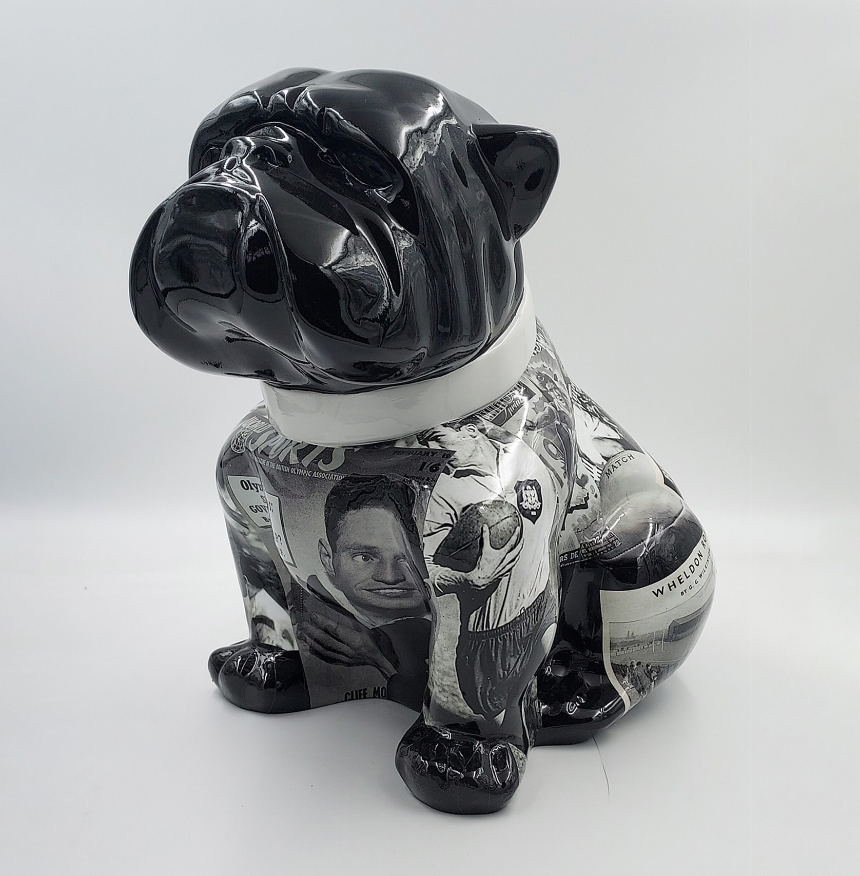 Bulldog Angelo 60cm dog - rugby 1 Ceramic dog statue with a glossy black head, white collar, and body covered in black and white newspaper clippings.