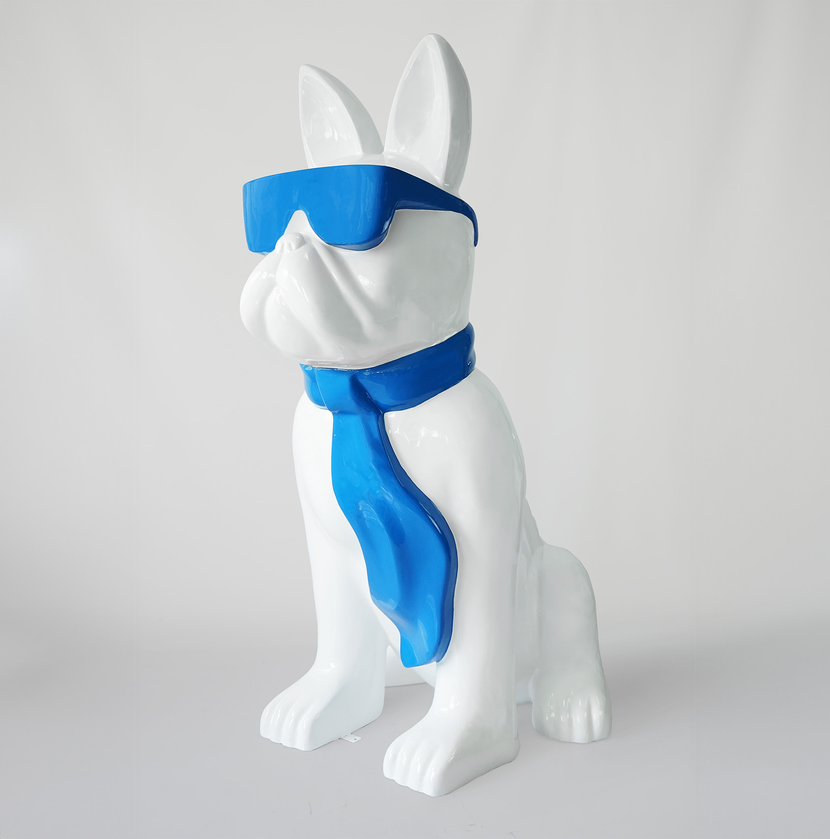 Large figure of a bulldog with a tie and glasses - blue sky 1 White statue of a dog wearing blue sunglasses and a blue scarf.