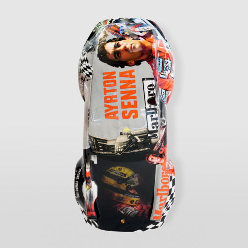 Model car decorated with images and text related to Ayrton Senna, including his name, face, race scenes, and sponsor logos.