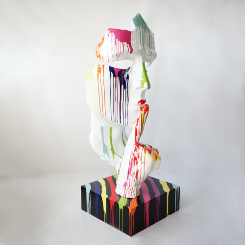 Sculpture of a face with a hand gesturing for silence, covered in vibrant, dripping paint on a painted base.