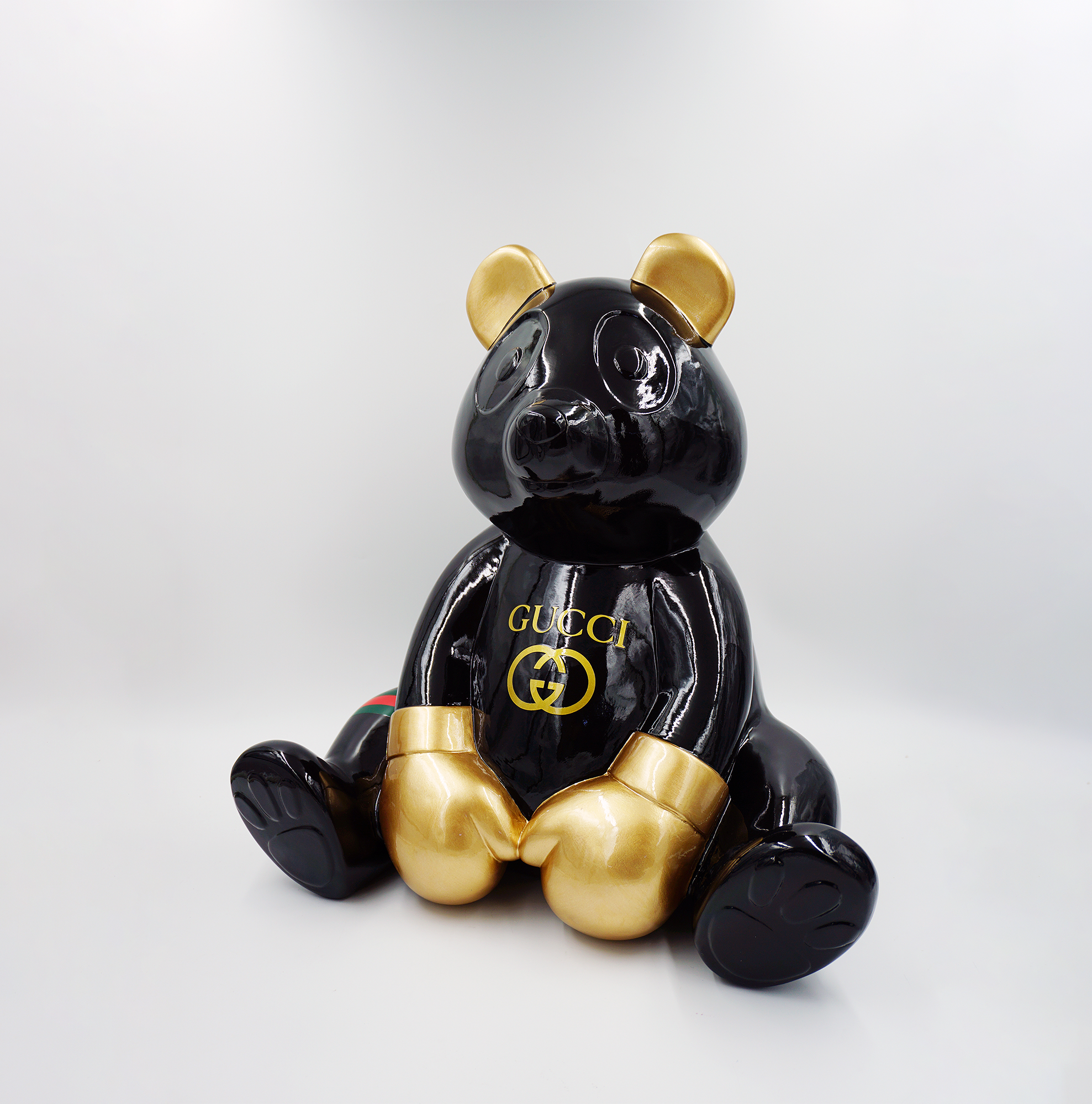 Panda G 1 A black glossy teddy bear sculpture with gold accents on its ears, hands, and feet, featuring the