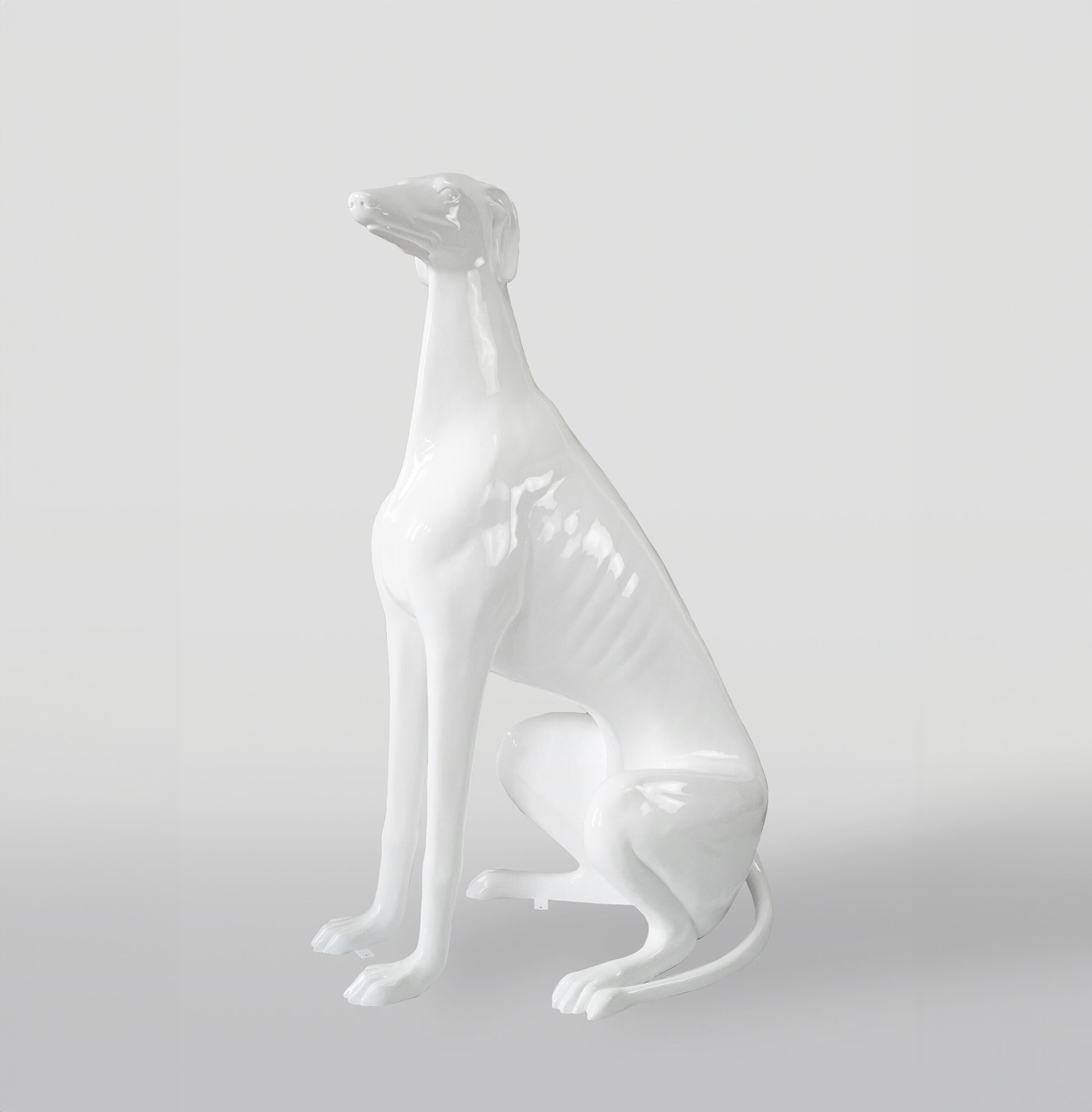 The large figure white greyhound 1 White glossy statue of a sitting dog with a sleek and elegant body shape.