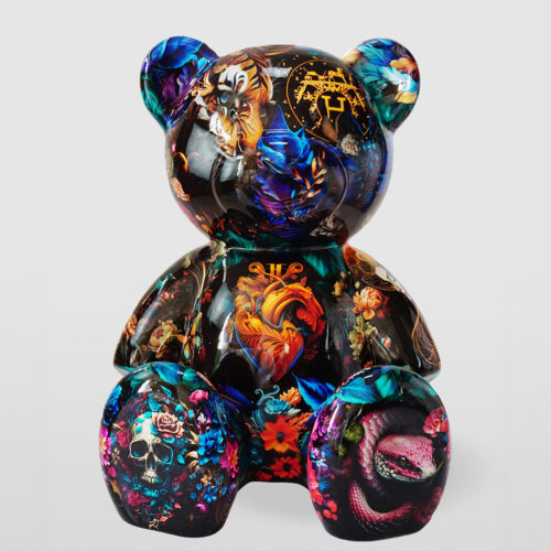 Kolorowa figurka misia z bogatym, kwiatowo-zwierzęcym wzorem na czarnym tle.