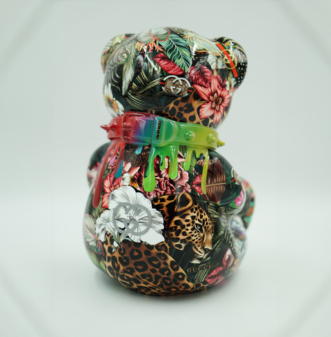 Kolorowy ceramiczny miś ozdobiony motywami roślinnymi i zwierzęcymi, z neonową obrożą na szyi.