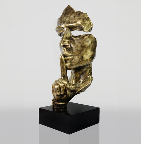 Bronze sculpture of a face with a finger to its lips mounted on a black rectangular base.