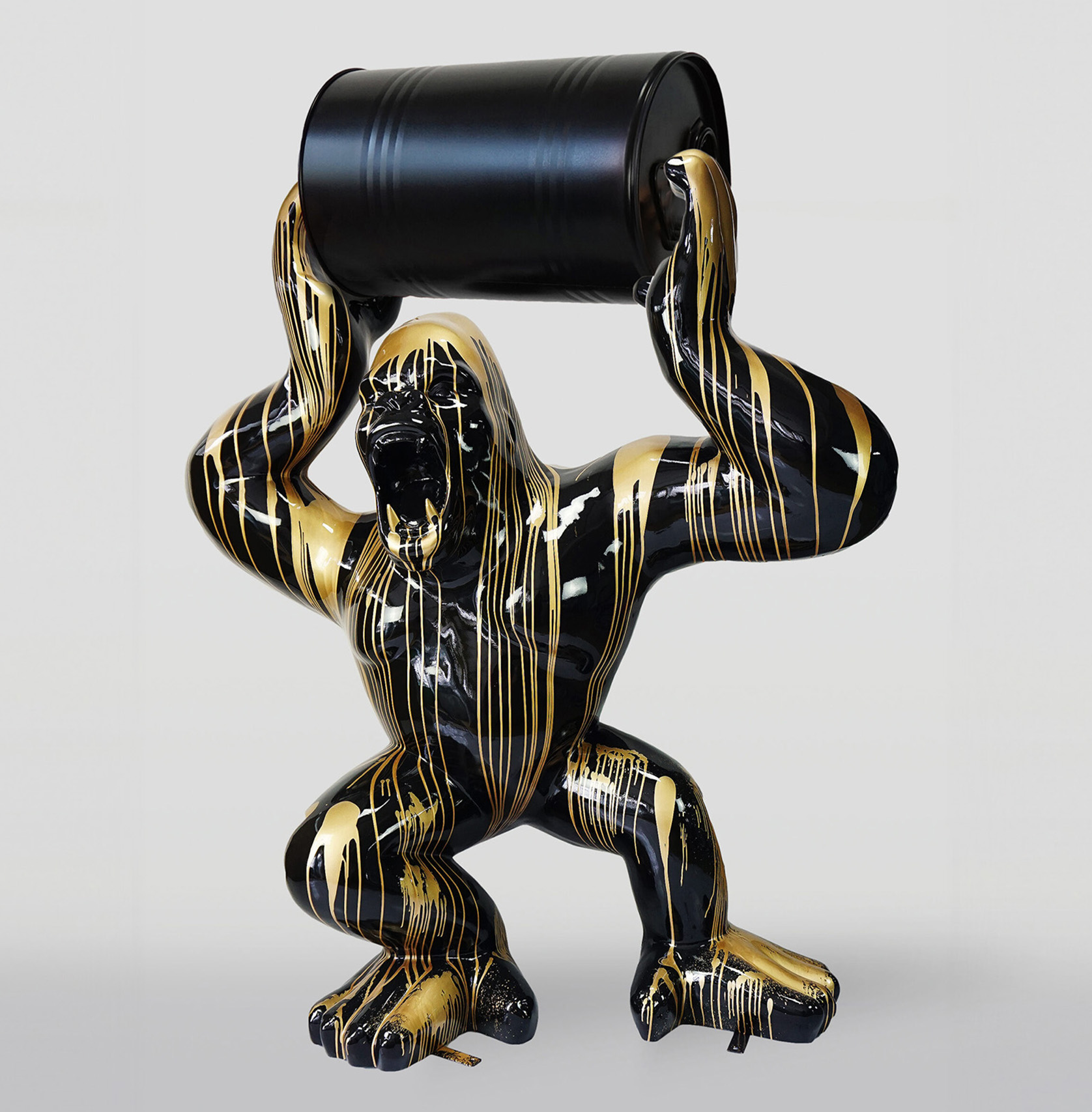 Large gorilla figure with golden trash barrel 1 Sculpture of a black and gold gorilla holding a black barrel above its head.
