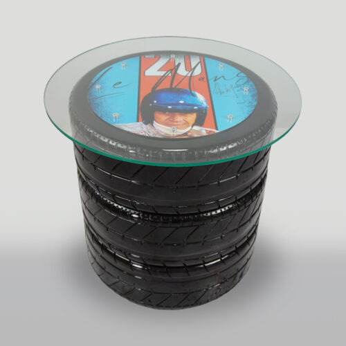 Glass table with a base made of stacked tires, featuring a circular artwork under the glass depicting a person in a racing helmet and the text 