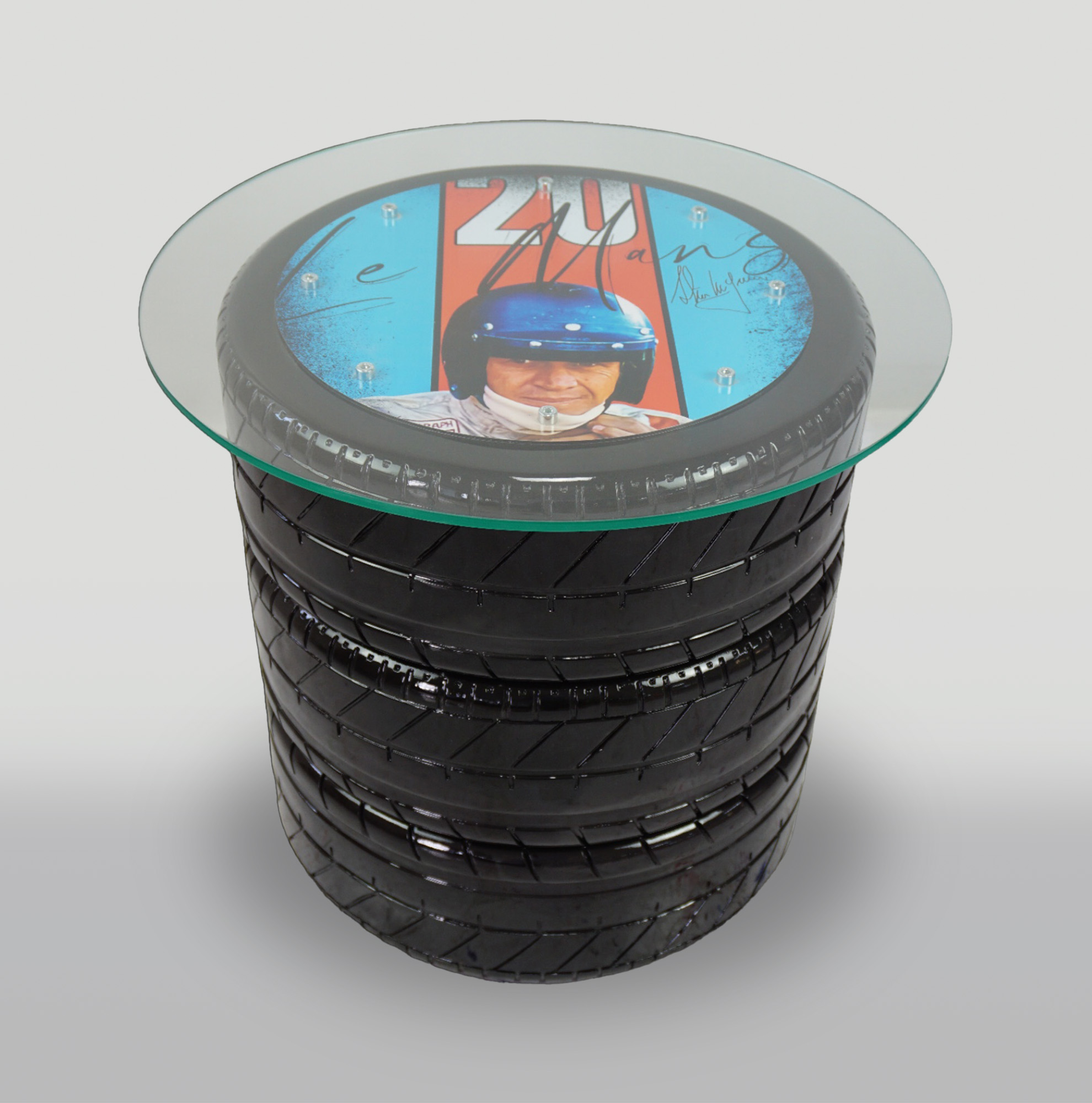 Table with tires with Le Mans 20 theme 1 Glass table with a base made of stacked tires, featuring a circular artwork under the glass depicting a person in a racing helmet and the text