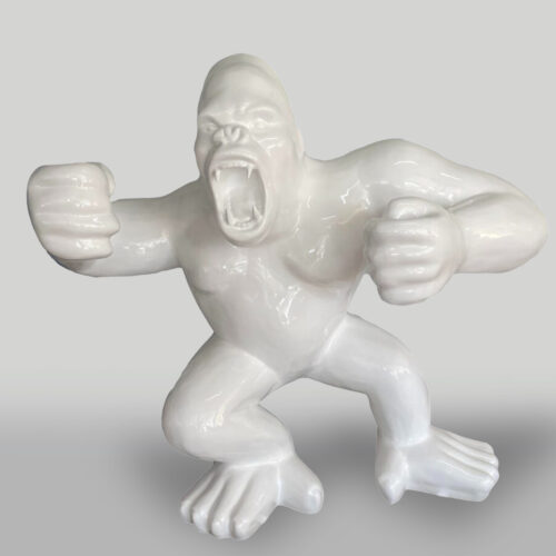 A white ceramic sculpture of an angry gorilla with its mouth open and fists clenched, in a crouched position.