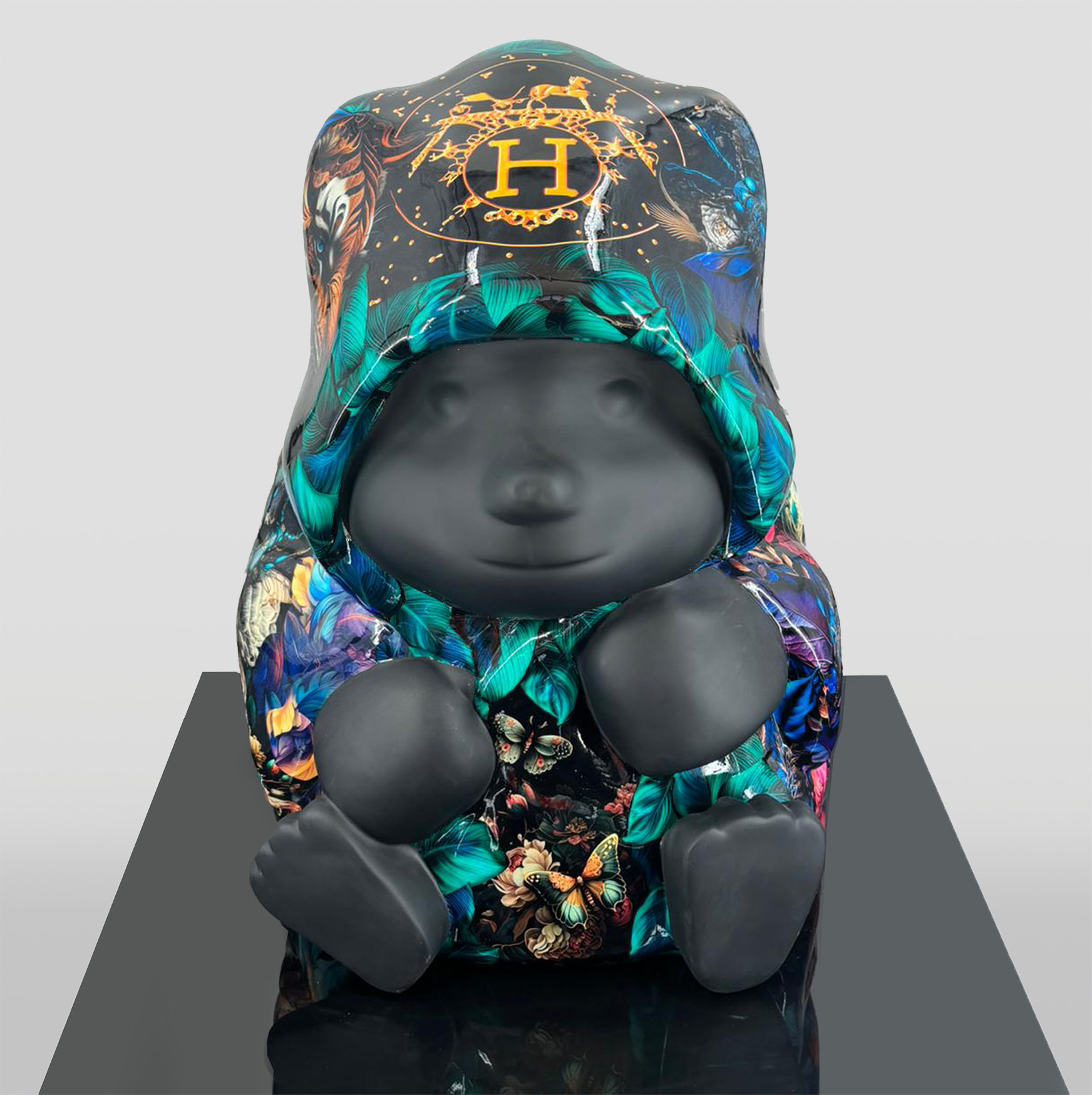 Sculpture of a bear-like figure with a black matte finish, wearing a colorful coat adorned with butterfly and foliage patterns and an emblem featuring an 