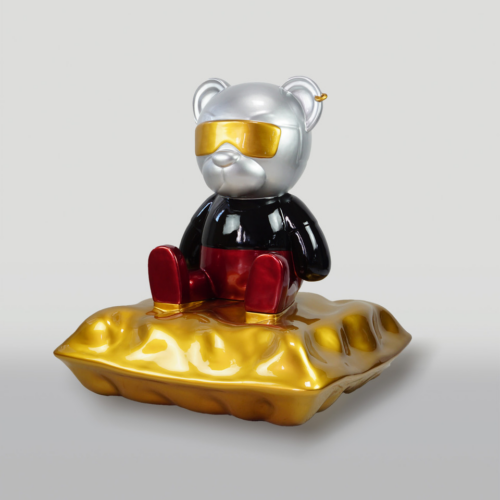 A metallic bear figure wearing yellow sunglasses, a black shirt, and red pants, sitting on a golden cushion.