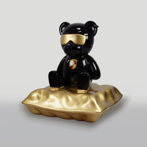 A black bear statue with gold sunglasses, seated on a plush gold pillow, featuring a Porsche logo on its chest.