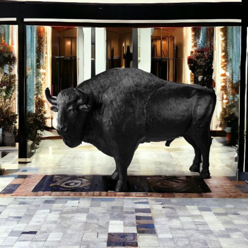 A buffalo standing inside a brightly-lit, ornate indoor hallway.