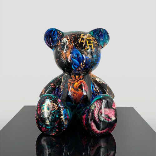 A black teddy bear sculpture with vibrant, intricate, and colorful patterns including images of a snake, butterfly, flowers, and animal faces, displayed on a reflective surface.